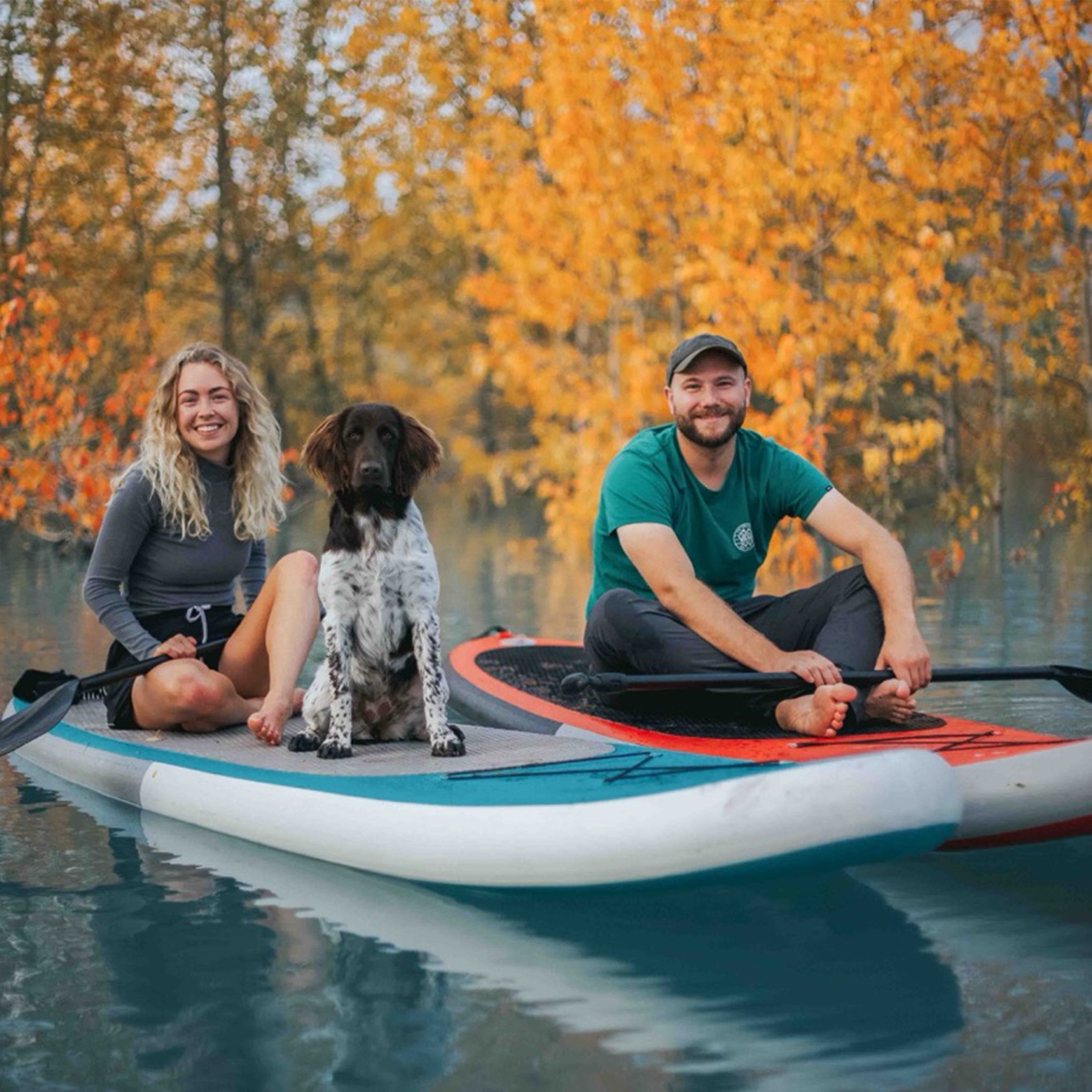 Couple paddleboarding with their dog on an autumn lake using a Synergy SUP board