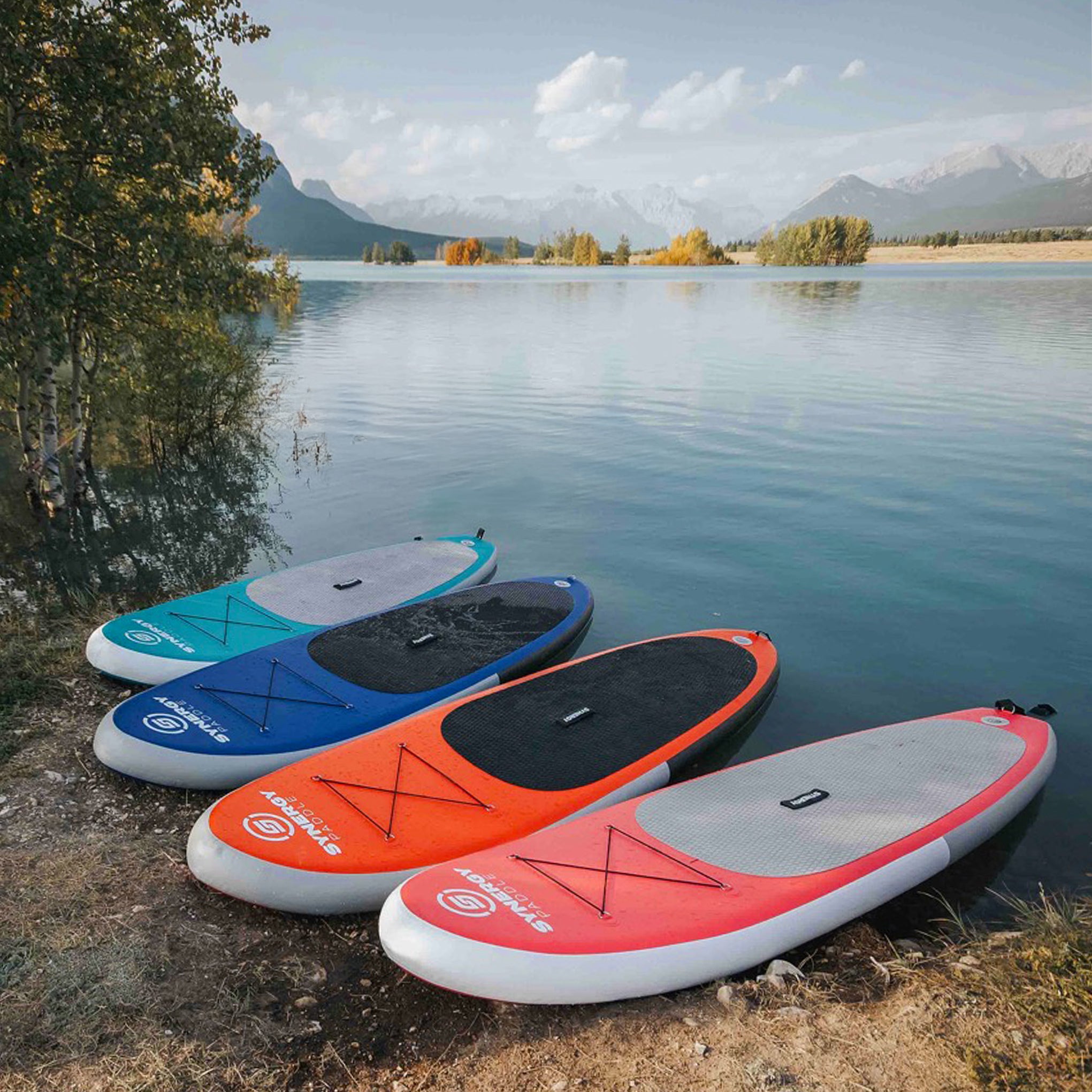 Synergy inflatable paddleboards in multiple colors displayed by a scenic lake view
