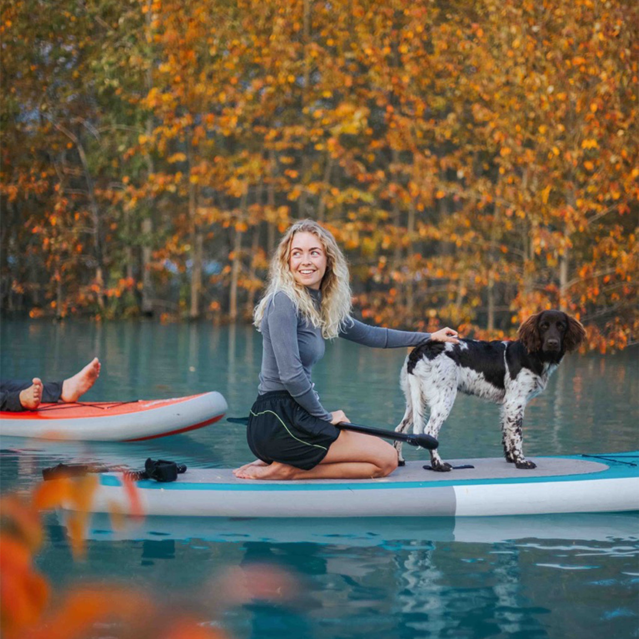 Woman paddleboarding with her dog on an autumn lake using a Synergy board